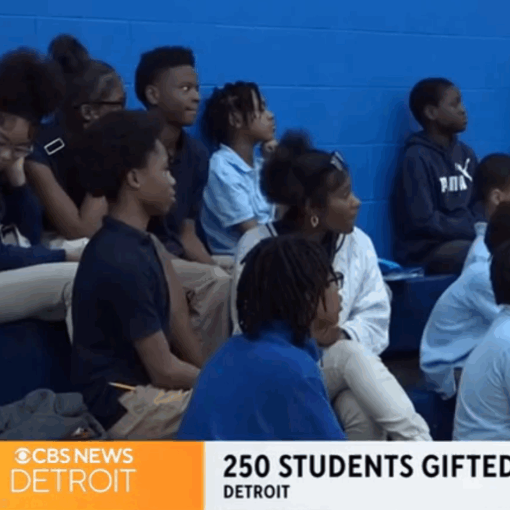 In a bustling gymnasium, Detroit students in uniforms listen attentively as the news banner reads, "250 Students Gifted - Detroit," with the CBS News Detroit logo. Excitement buzzes through the air like the anticipation before a Free Press Marathon race.