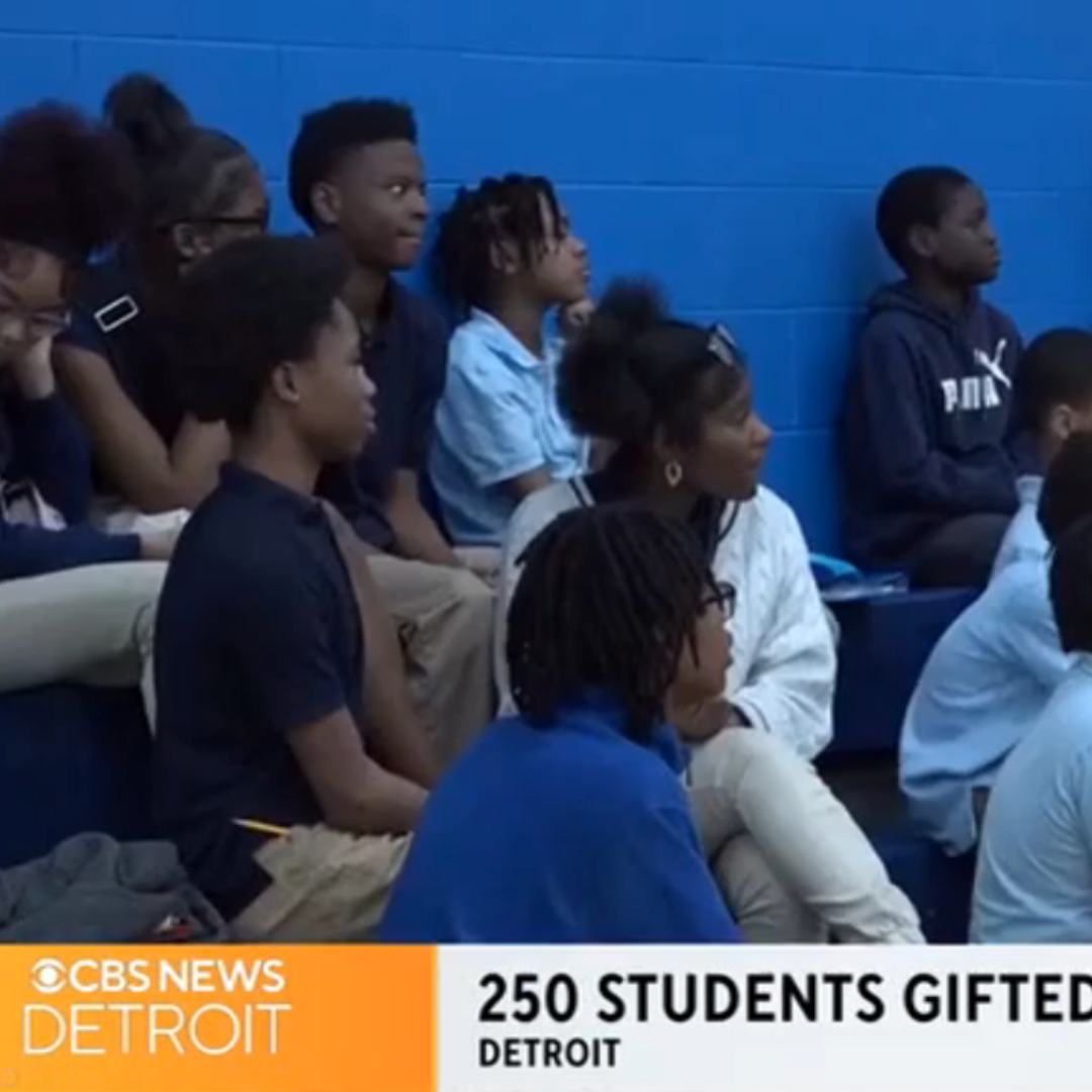 In a bustling gymnasium, Detroit students in uniforms listen attentively as the news banner reads, "250 Students Gifted - Detroit," with the CBS News Detroit logo. Excitement buzzes through the air like the anticipation before a Free Press Marathon race.