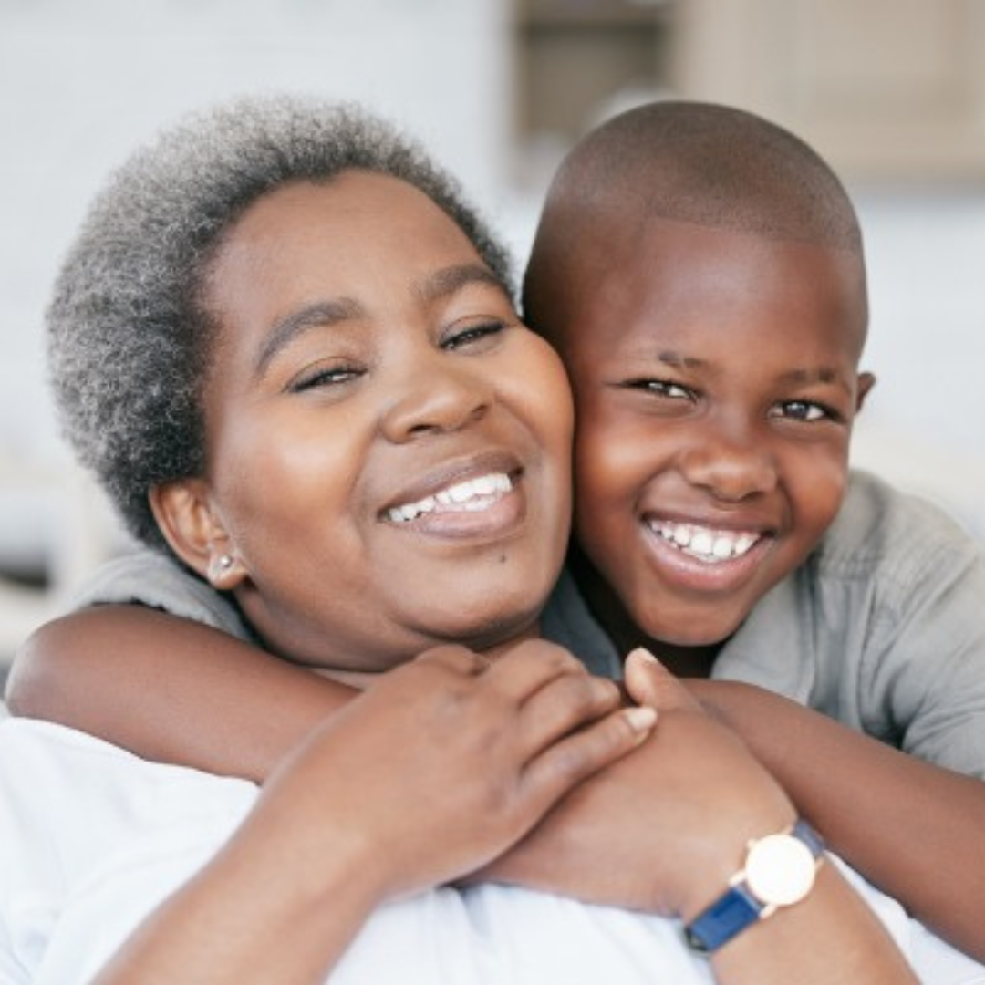 Anna and a young boy are smiling, the boy hugging her from behind. They both look joyful in a well-lit indoor setting, capturing a beautiful moment that seems like it's right out of Anna's Story.